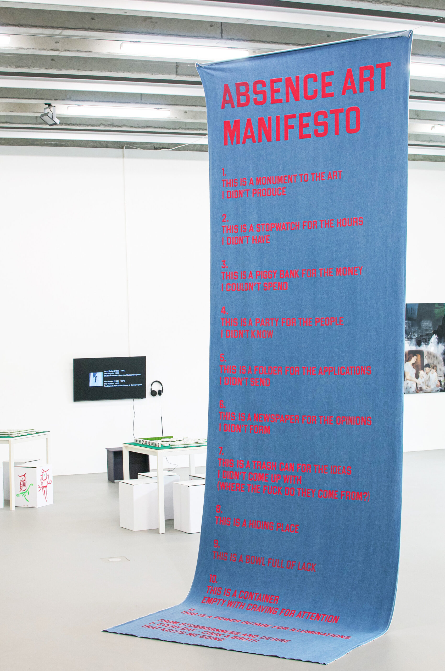 Large blue denim fabric hanging from the ceiling. Screenprinted red letters stating "Absence Art Manifesto" and 11 claims.