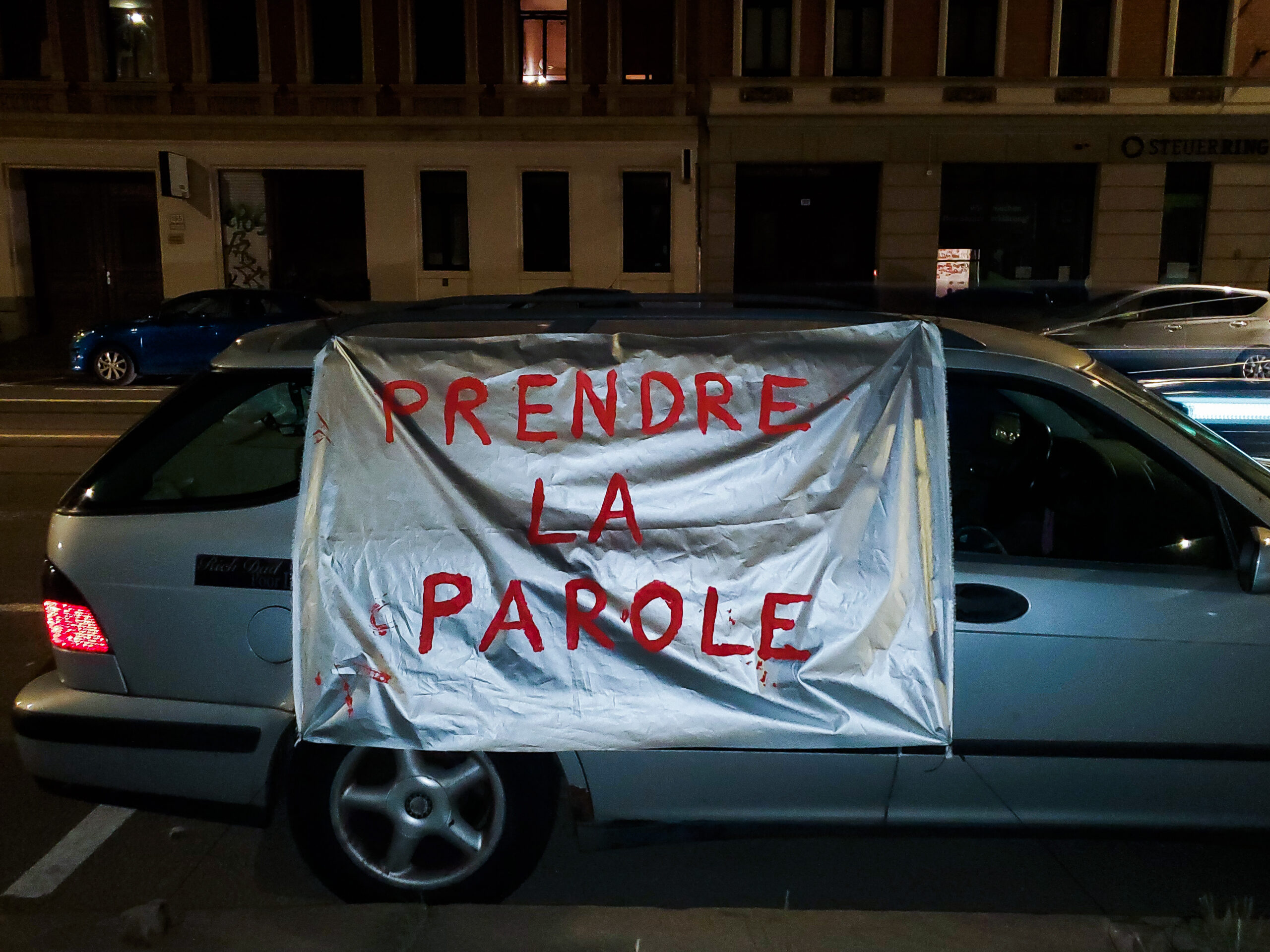 Car of artist Laura Mahnke carrying a silver banner that says Prendre la parole in red letters